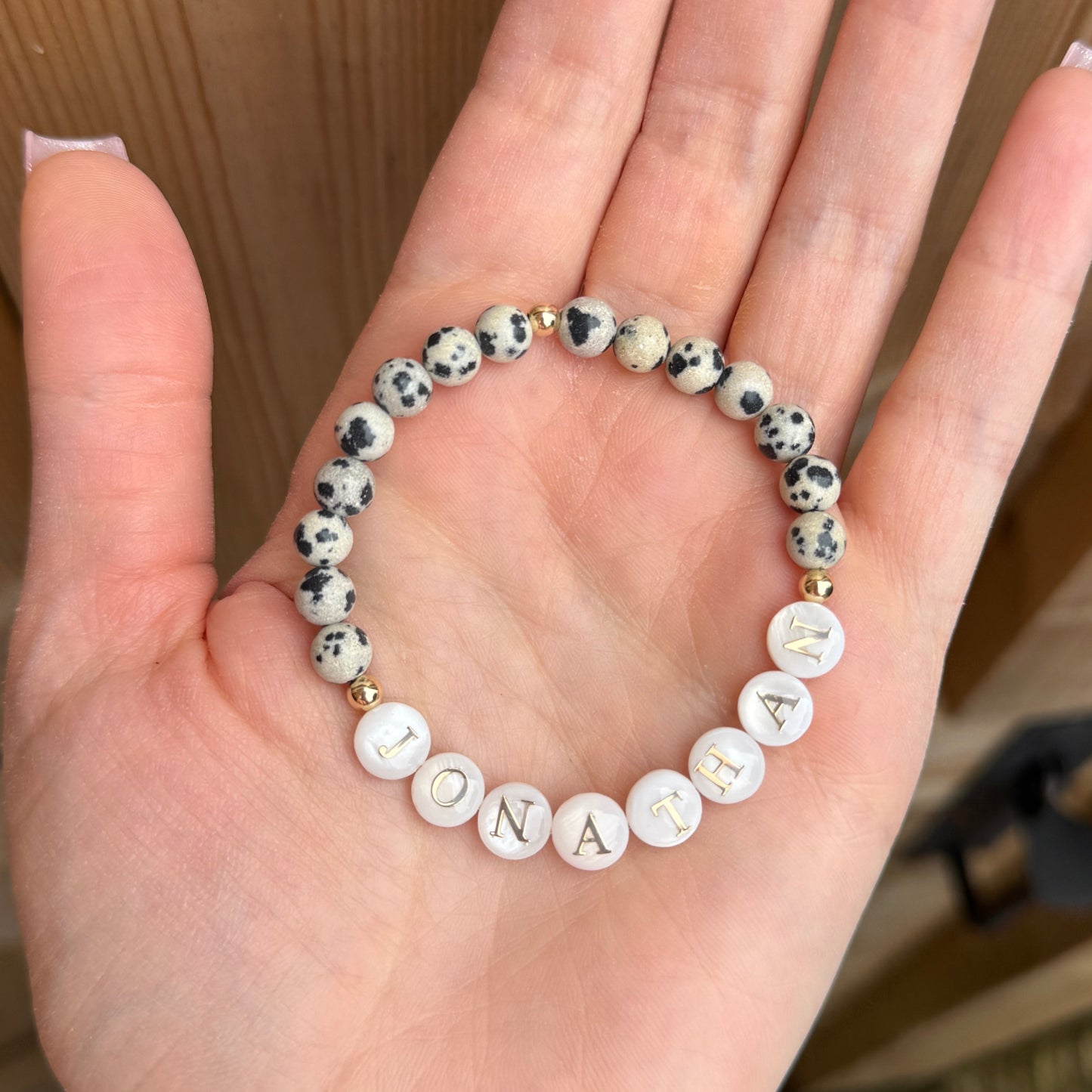 Hand holding beaded bracelet with pearl lettering against a wooden background