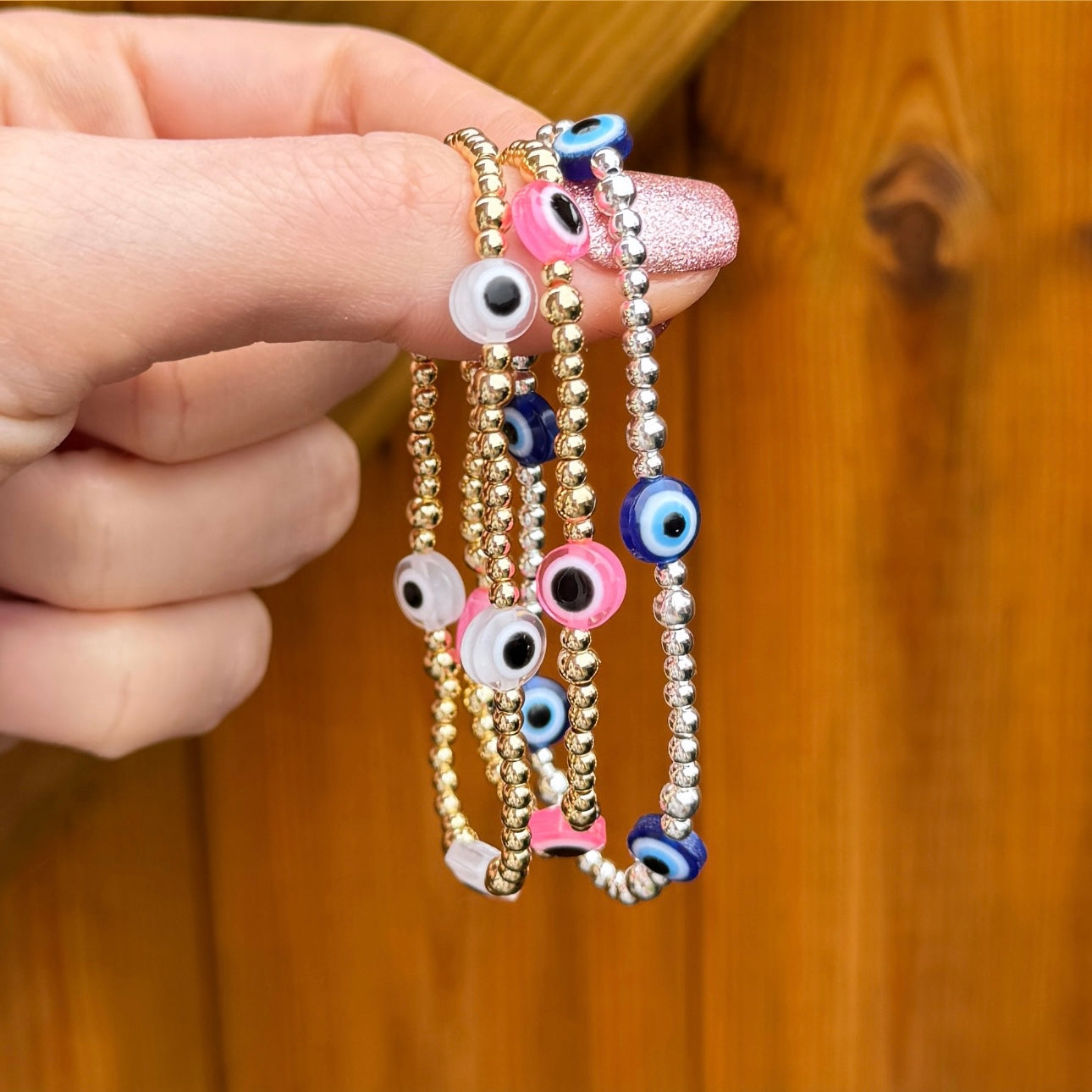 Hand holding a stack of evil eye bracelets in pink, clear and blue options